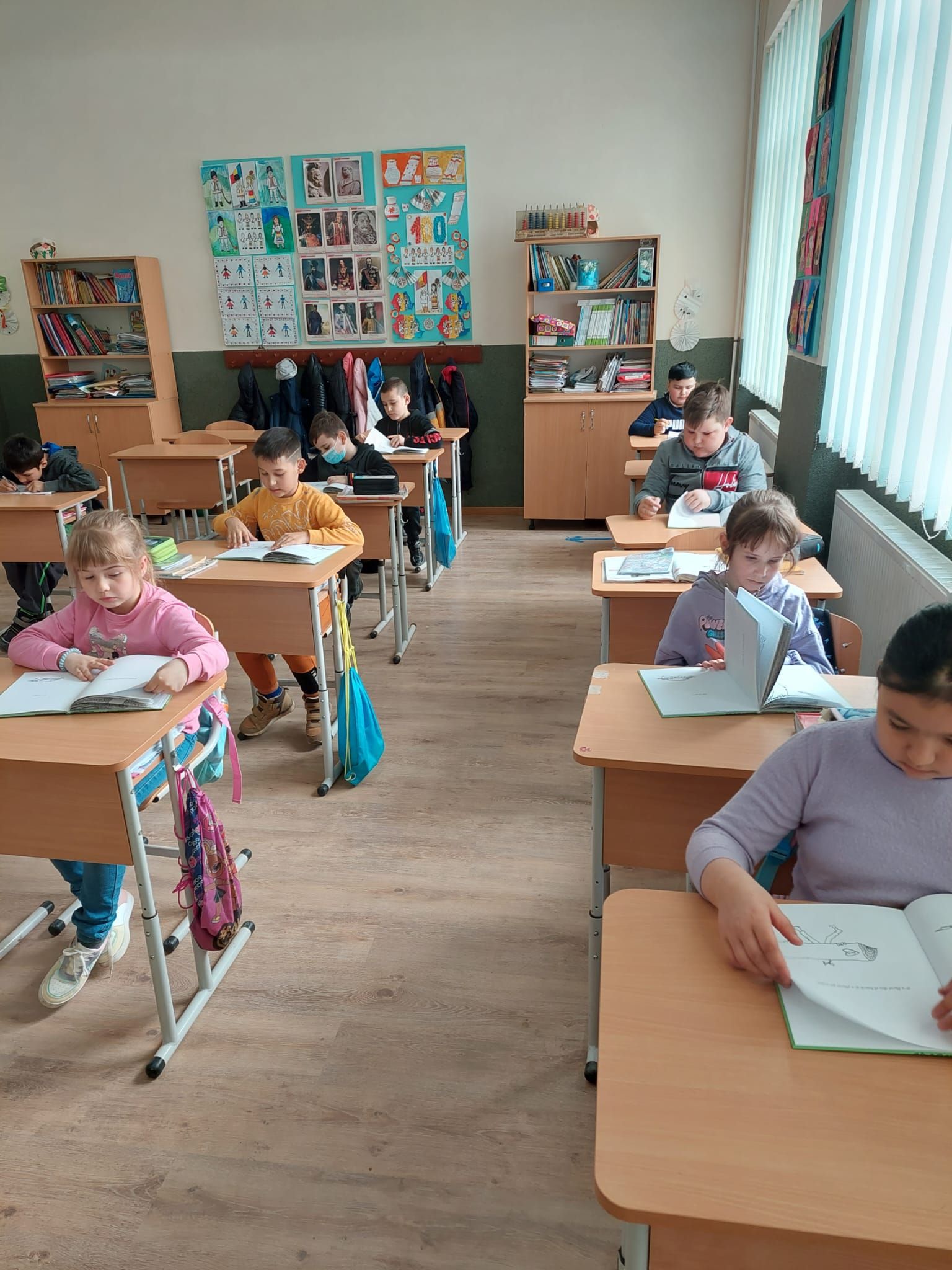 Elevi din clasele mici citind în bănci, într-o sală de clasă luminoasă