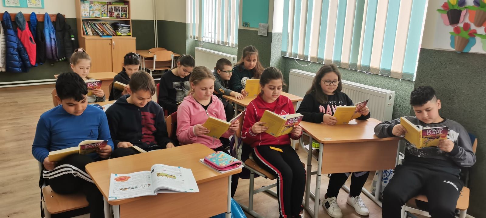 Elevi așezați în semicerc, citind cărți cu coperte galbene
