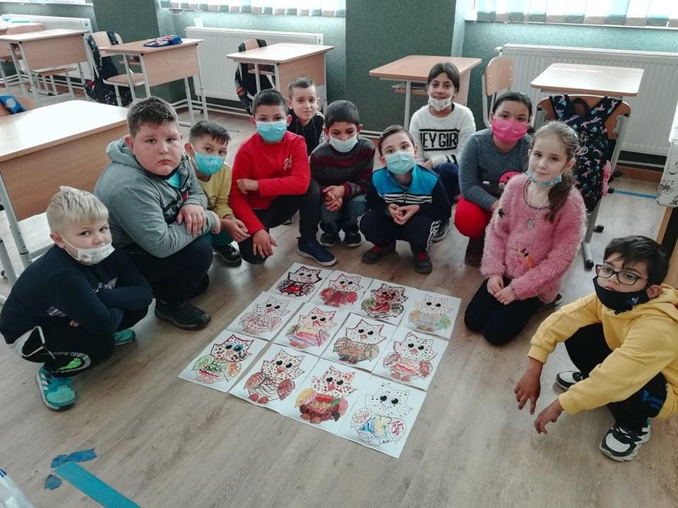 Elevi așezați pe podea în jurul desenelor lor cu bufnițe