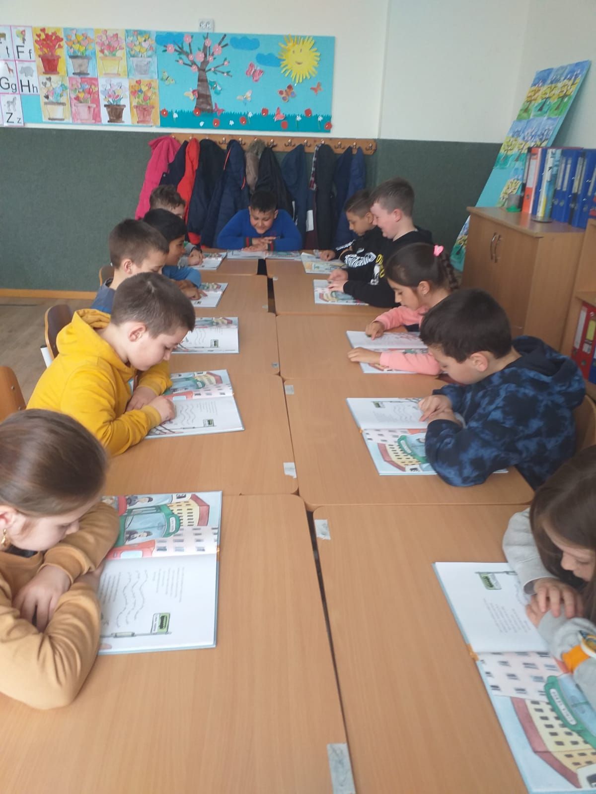 Elevi la mese alăturate, citind din cărți ilustrate