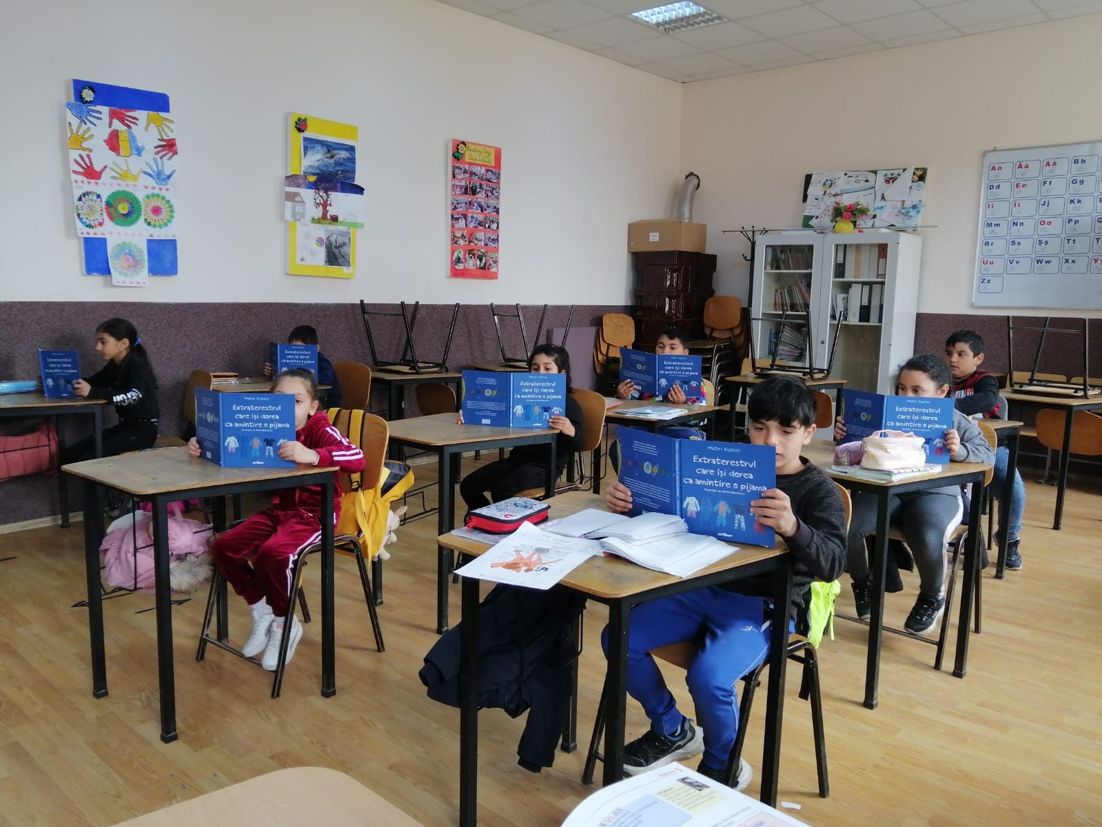 Elevi în bănci, fiecare cu un exemplar din aceeași carte albastră