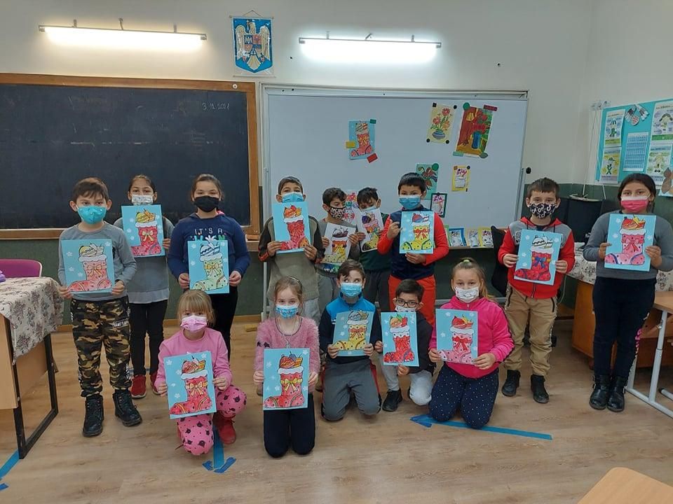 Elevi din clasele primare, cu măști de protecție, care își arată desenele de iarnă
