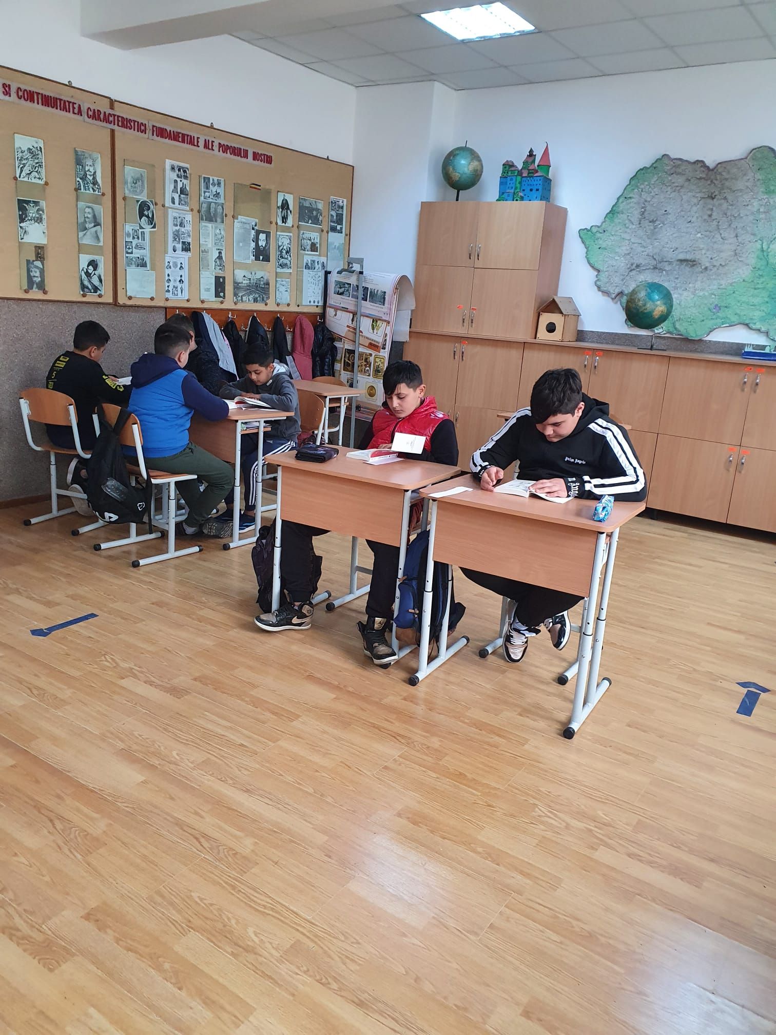 Elevi mai mari scriind și citind în bănci, într-o sală cu o hartă pe perete