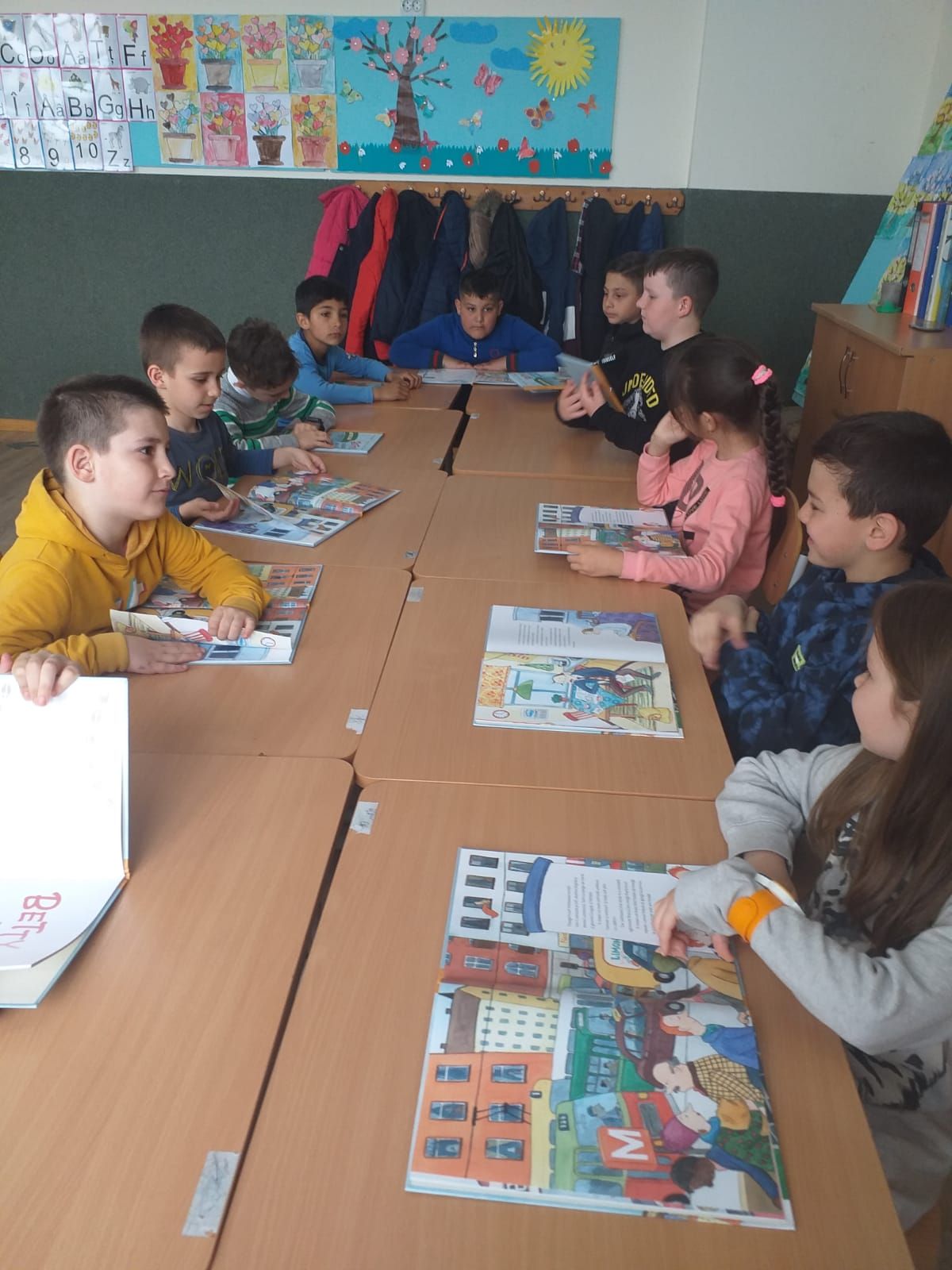 Elevi răsfoind cărți ilustrate la mesele din clasă