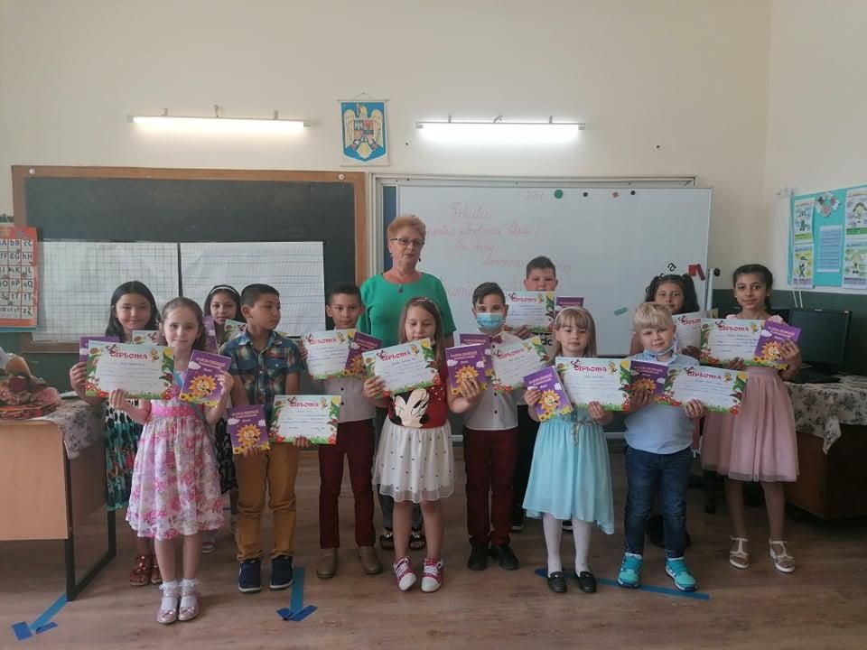 Elevi din clasele primare cu diplome și cărți, alături de un cadru didactic