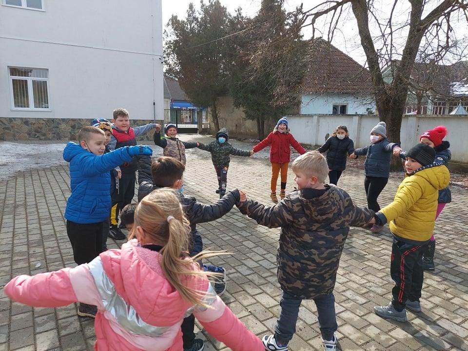 Elevi ținându-se de mână într-un joc în cerc, în curtea școlii, iarna