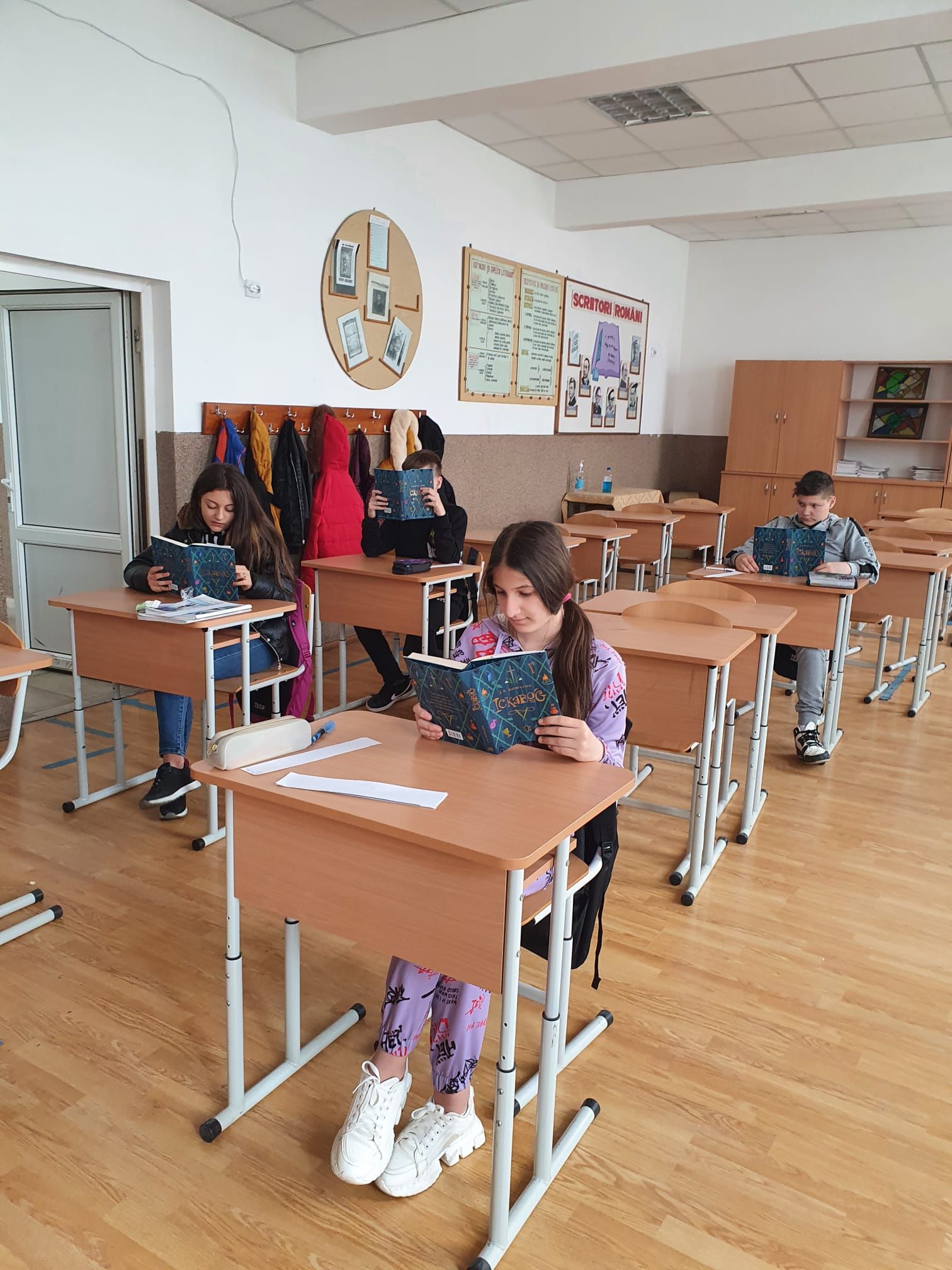 Elevi citind cărți cu coperte închise la culoare, fiecare la câte o bancă